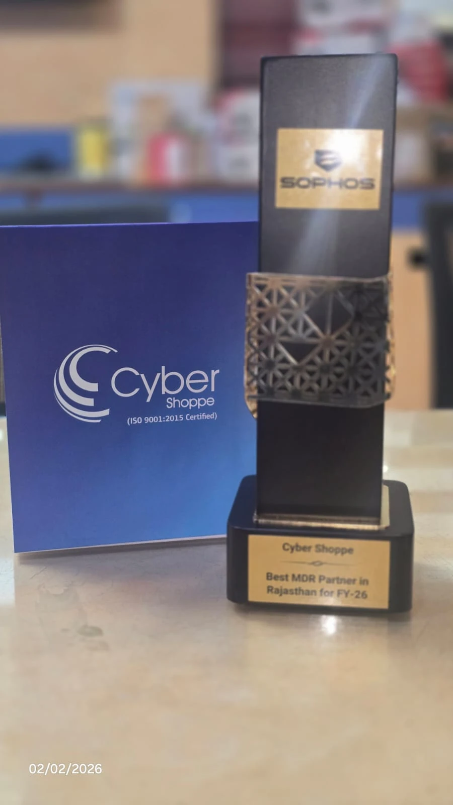 A black and gold Sophos trophy engraved "Cyber Shoppe — Best MDR Partner in Rajasthan for FY-26", standing beside a Cyber Shoppe folder.