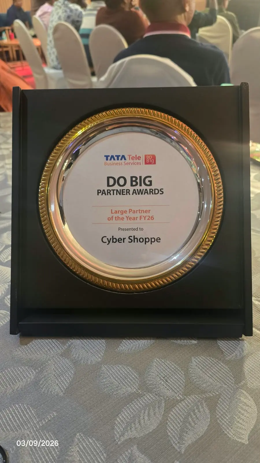 A gold-rimmed silver plate in a black stand reading "Tata Tele Business Services, DO BIG Partner Awards, Large Partner of the Year FY26, presented to Cyber Shoppe".