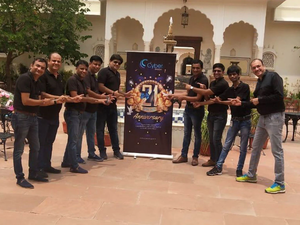 The team pointing at a banner marking Cyber Shoppe's 21st anniversary.