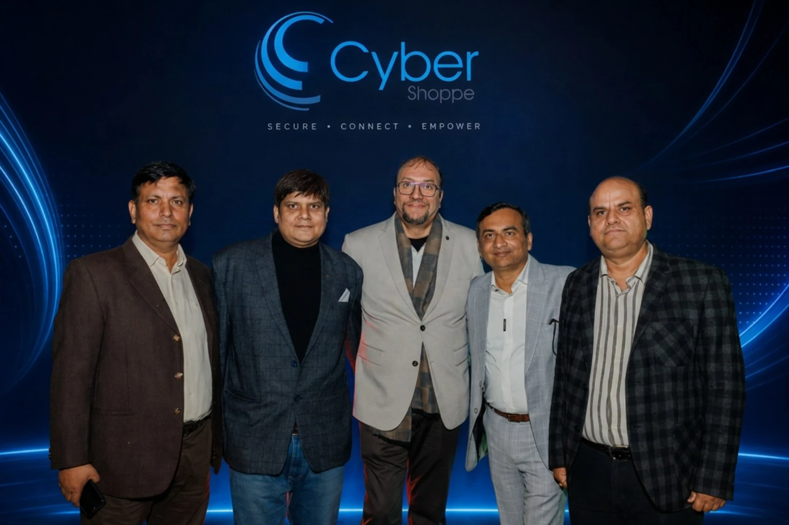 Five members of the Cyber Shoppe team standing together in front of a lit branded backdrop reading Cyber Shoppe — Secure · Connect · Empower.